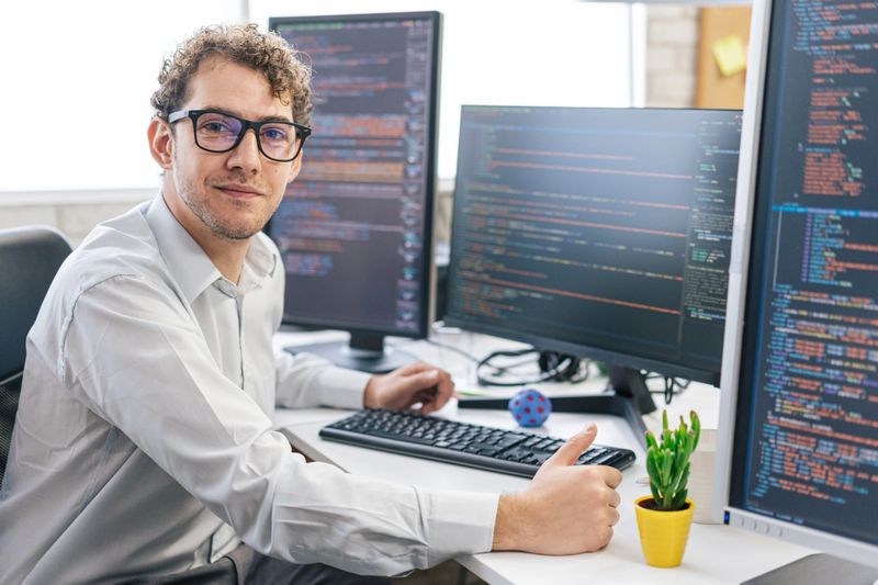 Portrait of young smiling female programmer, sitting on her desk with computers in an IT office