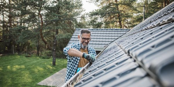 Man cleaning roof gutters outdoors.