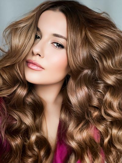 Close-up of a woman with voluminous, wavy light brown hair and natural makeup.