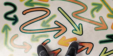 Person wearing black sneakers stands on a floor with colorful arrows pointing in multiple directions