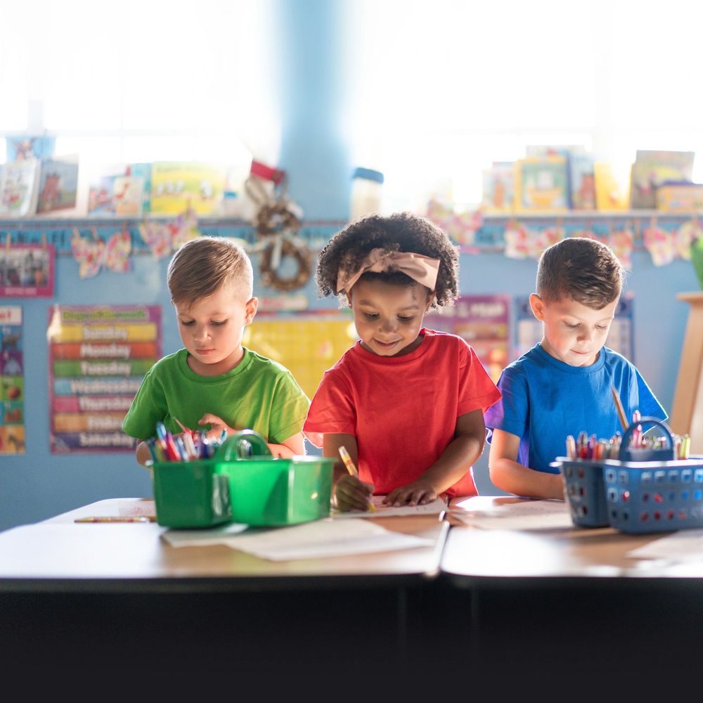 Three young children focused on coloring at a classroom table.