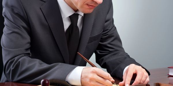 A man in a suit writing with a pen at a desk.