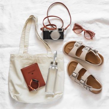 Flat lay of travel essentials including a tote bag and sandals.
