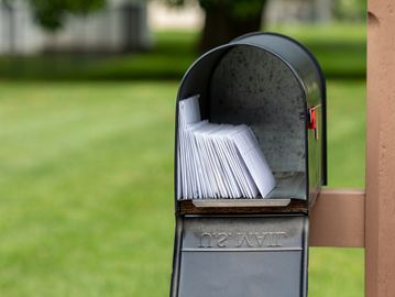 Mailbox stuffed with numerous white envelopes outdoors.