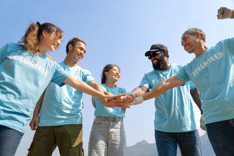 Group of happy multi-ethnic diverse volunteers joining hands stack together and raising hands with smile to show the power of unity in charity work, key to success in making future a better world