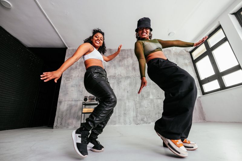 Two diverse stylish girls in the studio are dancing and moving to the music as they exercise their choreography.