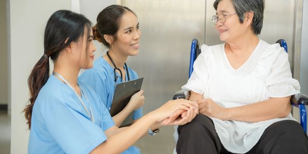 Two nurses speaking at eye level with a patient who is in a wheelchair.