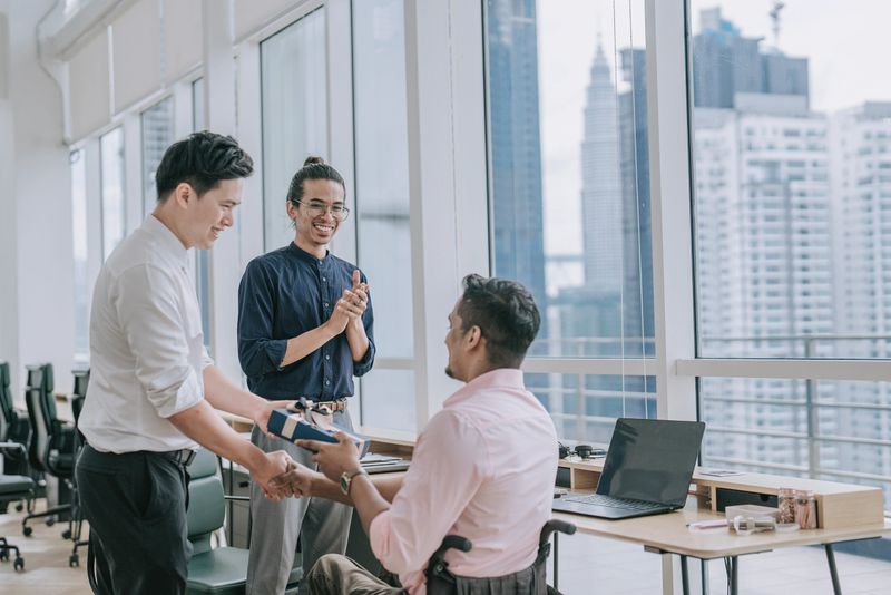 Asian Chinese manager congratulating and giving gift to coworker on performance achievement in office