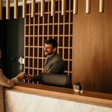 Recepcionista sonriente atendiendo a un cliente en un hotel.