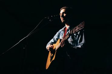 Musician passionately playing banjo on stage with eyes closed.