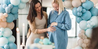 Two women at a baby shower with blue and beige balloons.