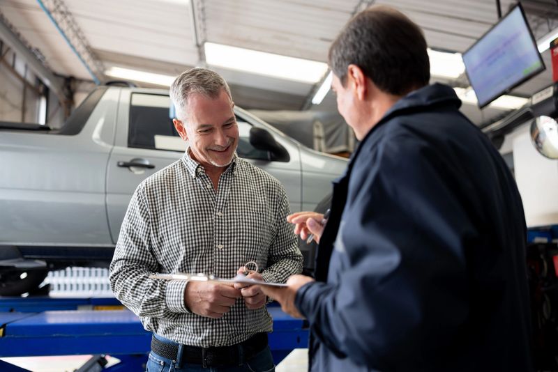 Happy man leaving his car at the garage and smiling while talking to the mechanic