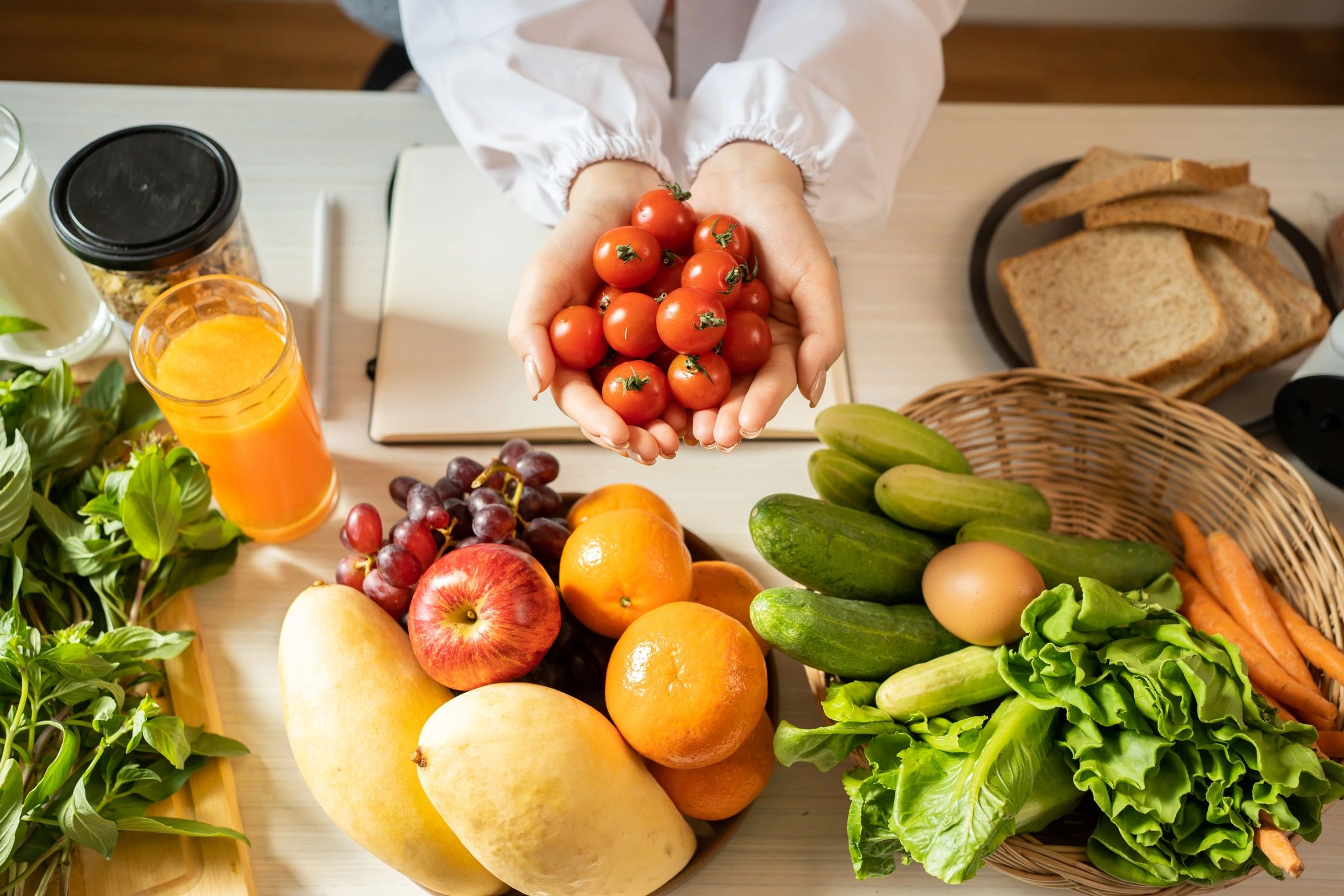 Hands holding cherry tomatoes with fresh fruits and vegetables on table.