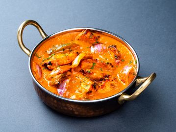 A bowl of creamy Indian butter chicken curry with herbs.