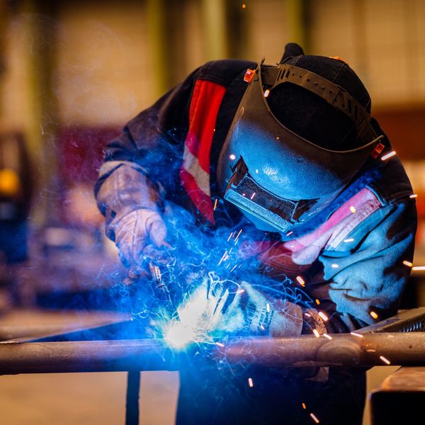 Welder in protective gear working with bright sparks and blue smoke.