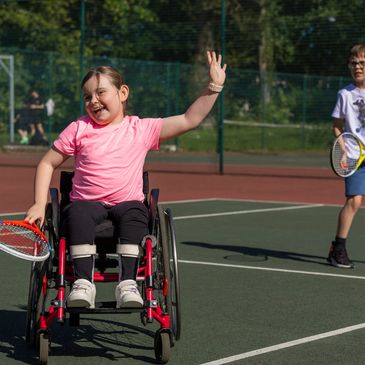 Smiling girl in wheelchair playing tennis.