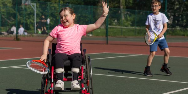 Smiling girl in wheelchair playing tennis outdoors.