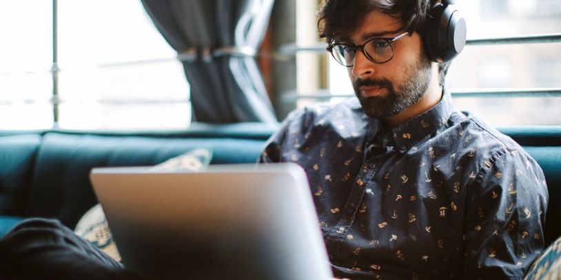 Man wearing headphones and glasses working on laptop.