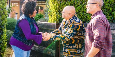 Three people warmly greeting each other outdoors.