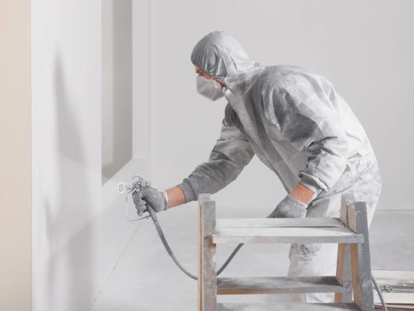 Person in protective suit spray painting a wall.