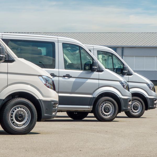 A row of white fleet vans parked side by side outdoors.