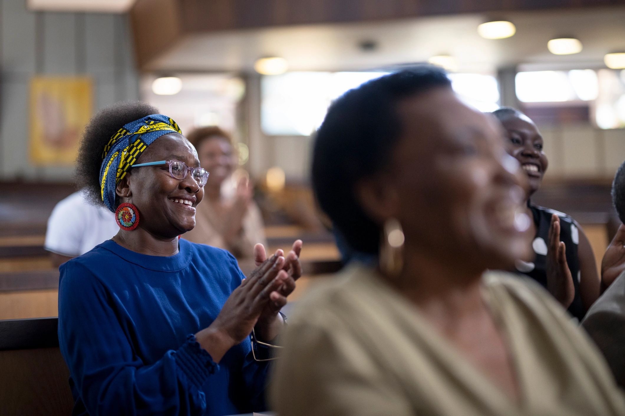 A group of women smiling and clapping in a communal indoor setting.