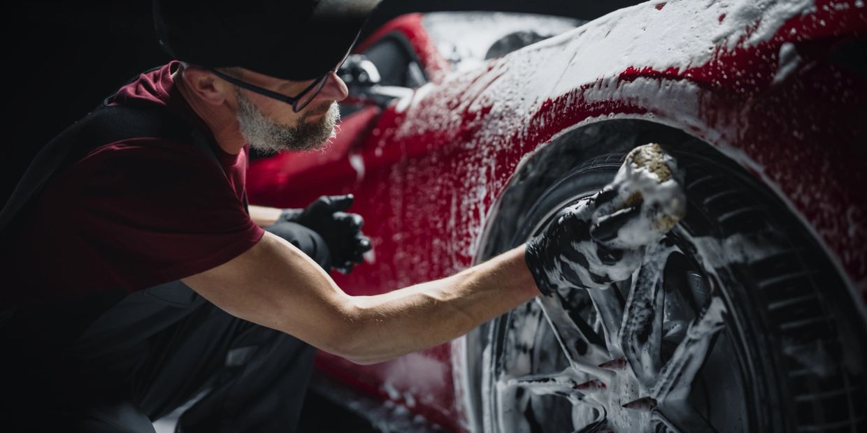 Man washing a red car's wheel with foam.