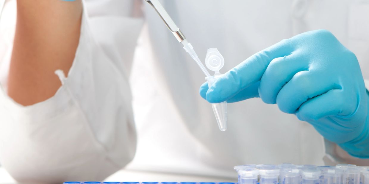 Scientist using a pipette to transfer liquid into a test tube in a lab.