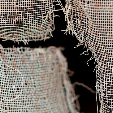 Close-up of torn, frayed fabric mesh against a black background.