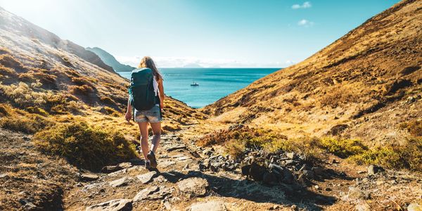 A woman hiking towards the ocean on a sunny day.