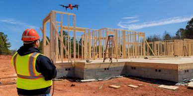 Construction worker operating a drone at a building site with wooden framing.