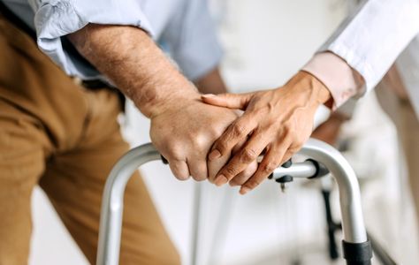 Elderly person using a walker with supportive hand on top.