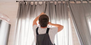 handyman adjusting gray curtains in a bright room.