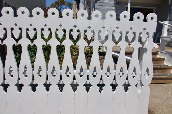 Decorative white wooden fence with intricate carved patterns in front of a house.