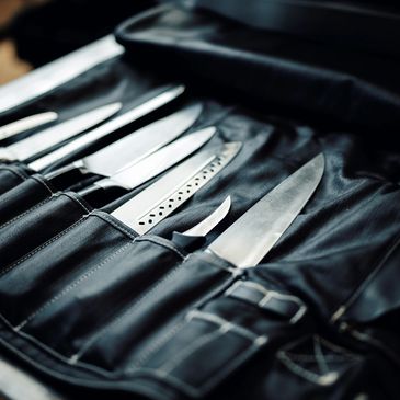A set of kitchen knives neatly arranged in a black leather knife roll.