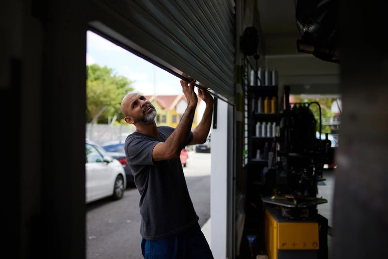 Asian male mechanic starts his day by opening shutter door to car workshop