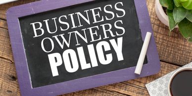 Chalkboard with "Business Owners Policy" written on it beside a cup of coffee and a plant.