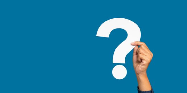 Hand holding a white question mark against a blue background.