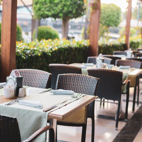 Outdoor restaurant seating with neatly set tables and wicker chairs.