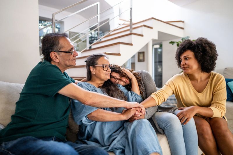 Young woman with her wife being comforted by her parents sitting on sofa in the living room at home
