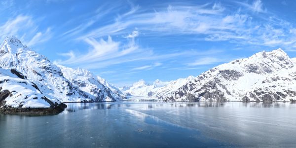 Snow-covered mountains surrounding a calm frozen lake under a blue sky.