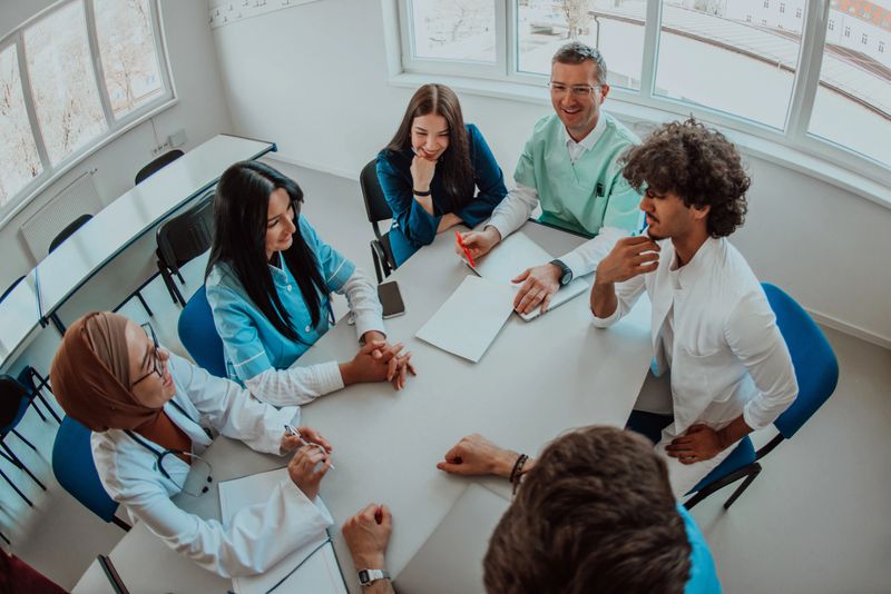 Top view of a group of multiethnic medical professionals including doctors, surgeons, and nurses are gathered in a hospital setting discussing patient care and using modern technology to address challenges in the medical field