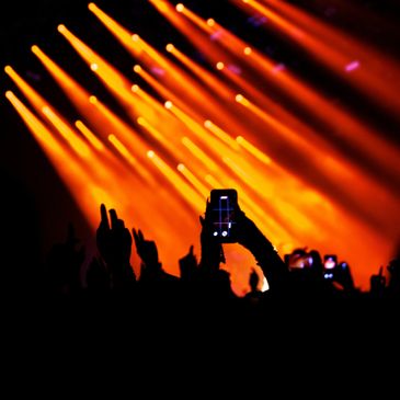 Crowd at a concert with orange stage lights and phones recording.