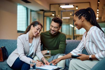 Three colleagues happily discussing and signing documents in an office.