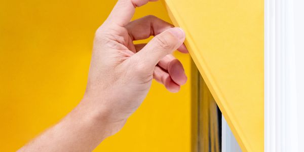 Hand lifting a yellow window blind.