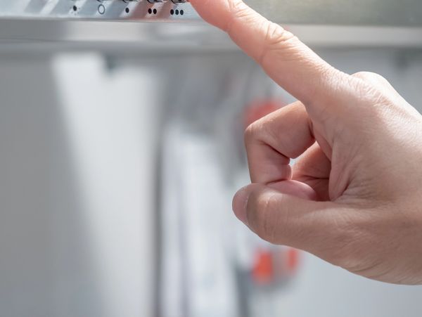 A hand pressing a button on an oven or microwave control panel.