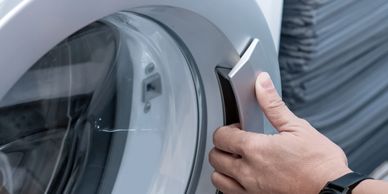 Hand opening the door of a front-loading washing machine.