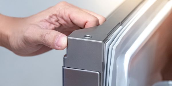 Hand adjusting a metallic appliance door hinge.