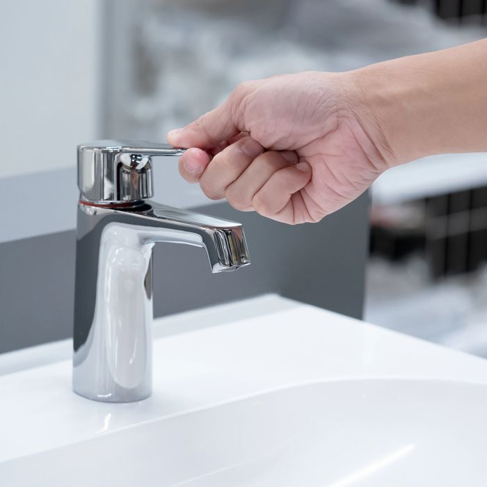 Hand turning on a modern chrome faucet above a white sink.