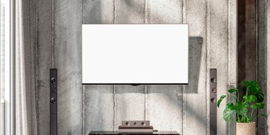 Modern living room with a blank TV screen and sleek speakers against a textured concrete wall.